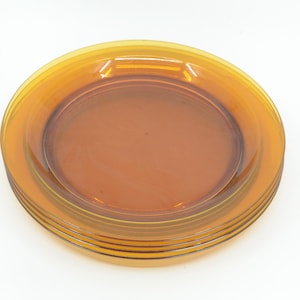 May include: A stack of amber-coloured, transparent plates. The plates have a slightly raised rim and a smooth, glossy surface. The plates are stacked on top of each other, with the top plate slightly smaller than the others.