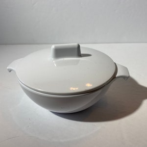 May include: White ceramic bowl with a lid. The bowl has a rounded shape and a small handle on the lid.