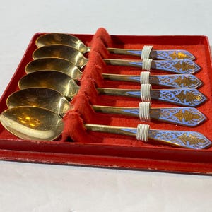 May include: Set of six silver teaspoons with blue and gold enamel designs in a red velvet box.