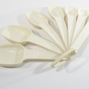 Puede incluir: Un juego de siete cucharas medidoras de plástico blanco, anidadas en forma de abanico. Las cucharas están etiquetadas con medidas en cucharaditas y cucharadas.