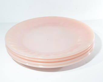 Puede incluir: Cuatro platos de vidrio rosa apilados uno encima del otro. Los platos tienen un borde ligeramente ondulado.