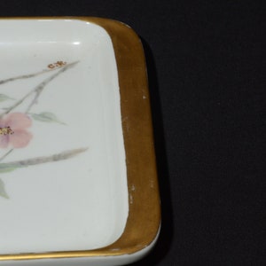 May include: Rectangular white ceramic tray with a gold-painted border. The tray features a floral design with pink flowers, green leaves, and brown stems. The corner of the tray has the initials "C.R." painted on it.