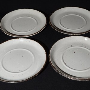 May include: Set of four white ceramic saucers with a brown rim and speckled glaze.