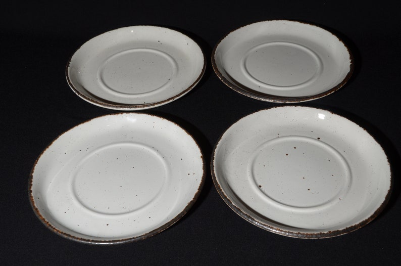 May include: Set of four white ceramic saucers with a brown rim and speckled glaze.