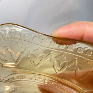 May include: A vintage amber glass bowl with a scalloped edge and an etched design. The bowl has a delicate floral pattern and a slightly wavy rim.