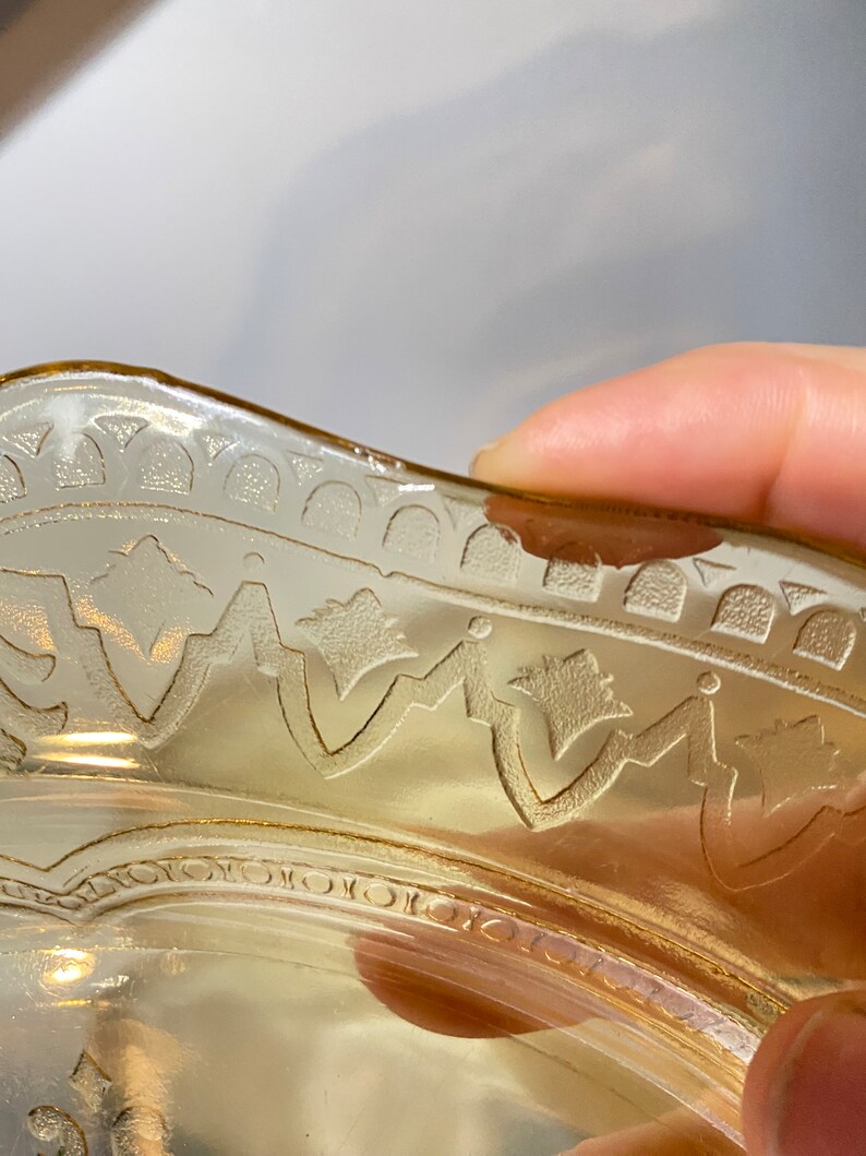 May include: A vintage amber glass bowl with a scalloped edge and an etched design. The bowl has a delicate floral pattern and a slightly wavy rim.