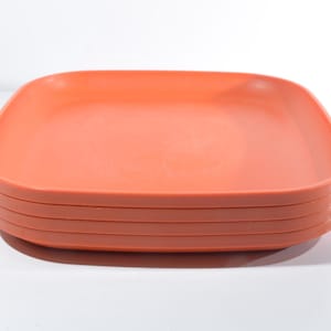Könnte beinhalten: Ein Stapel quadratischer, korallenfarbener Teller. Die Teller haben abgerundete Ecken und leicht erhöhte Ränder. Der Stapel besteht aus fünf Tellern, jeder mit einer glatten Oberfläche und einer einheitlichen Farbe. Die Teller sind aus einem haltbaren Material.