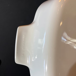 K&ouml;nnte beinhalten: Wei&szlig;e Keramik-Backform mit abgerundeter Form und einem Griff auf einer Seite. Die Form tr&auml;gt den Aufdruck "A-1-B 1 LITER" auf der Seite.