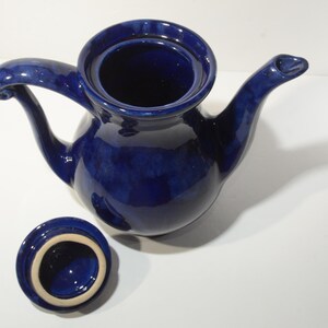May include: A cobalt blue ceramic teapot with a lid and a curved handle. The teapot has a rounded body and a spout.