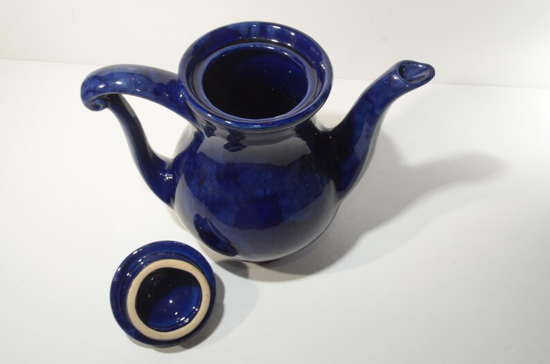 May include: A cobalt blue ceramic teapot with a lid and a curved handle. The teapot has a rounded body and a spout.