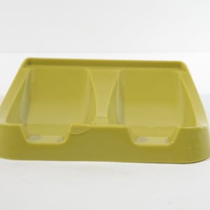 May include: A light olive green plastic soap dish with two compartments. The dish has a rectangular base with rounded corners and a slightly raised edge. The compartments are designed to hold two bars of soap. The dish is made of a durable plastic material.