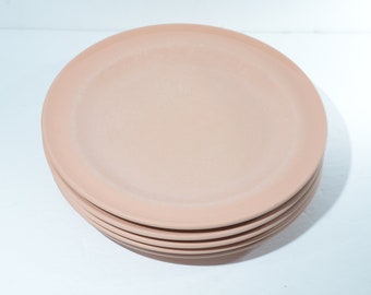 Könnte beinhalten: Ein Stapel von fünf runden, rosafarbenen Tellern. Die Teller haben ein schlichtes, minimalistisches Design und eine matte Oberfläche. Die Teller sind übereinander gestapelt, wobei der oberste Teller leicht angewinkelt ist.