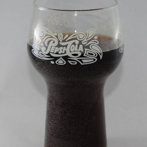 May include: A glass with a white Pepsi-Cola logo on the side, filled with a dark brown carbonated beverage.