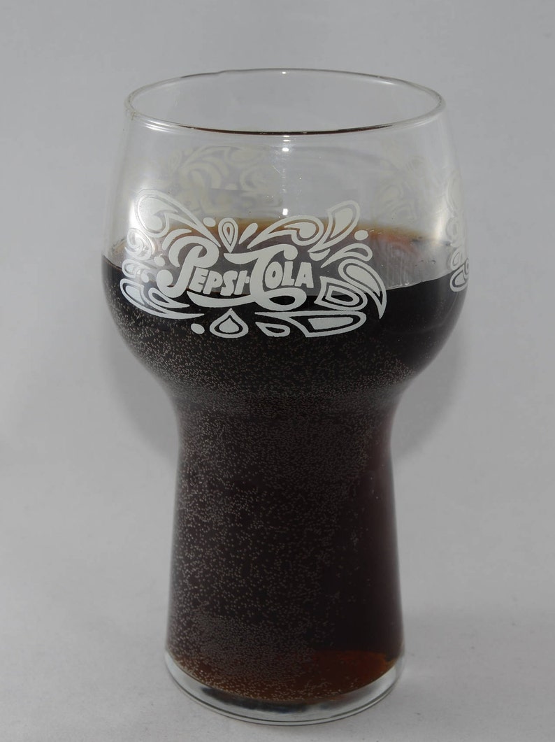 May include: A glass with a white Pepsi-Cola logo on the side, filled with a dark brown carbonated beverage.