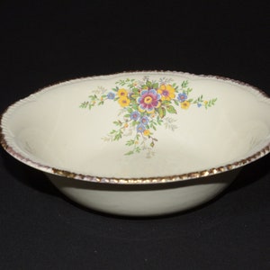 Pode incluir: Uma tigela de cerâmica branca com uma borda dourada e um desenho floral em tons de amarelo, azul, rosa e verde.