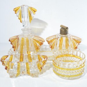 May include: A vintage glass perfume bottle set with a clear glass base and amber colored accents. The bottles have a decorative, ruffled design and are perfect for displaying on a vanity or dresser.