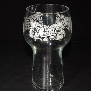 May include: A clear glass drinking glass with a wide base and a flared top. The glass has a white etched design of the Pepsi-Cola logo and swirls.