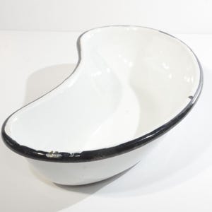 May include: White enamel kidney dish with a black rim. The dish has a slight chip on the rim.