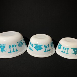 May include: Three white mixing bowls with a blue and white kitchen design. The bowls are nested together, with the largest bowl in the back and the smallest bowl in the front.