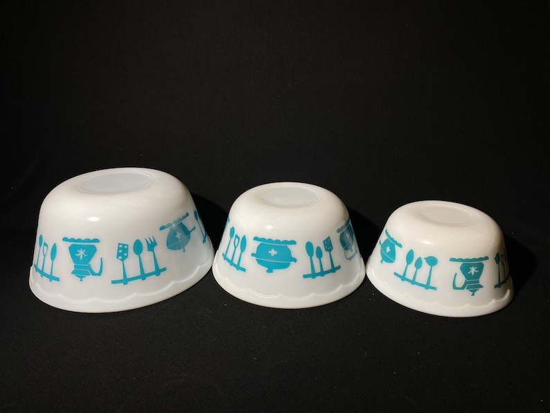 May include: Three white mixing bowls with a blue and white kitchen design. The bowls are nested together, with the largest bowl in the back and the smallest bowl in the front.