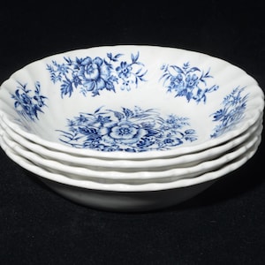 May include: A stack of four white ceramic bowls with a blue floral pattern. The bowls have a scalloped edge and a detailed blue floral design on the inside. The bowls are stacked on top of each other.