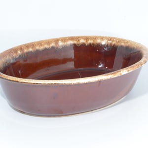 Könnte beinhalten: Ovale, braune Keramik-Servierschale mit glänzender Oberfläche. Der Rand hat eine hellere, gesprenkelte braune und beige Farbe. Die Schale hat ein schlichtes, klassisches Design, geeignet für verschiedene kulinarische Zwecke. Ca. 25 cm lang.