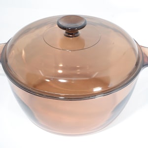 May include: An amber-tinted glass casserole dish with a matching lid. The dish features two side handles and a round lid with a small knob. This oven-safe cookware is suitable for cooking and serving food.