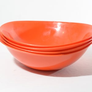 May include: Four orange plastic bowls stacked on top of each other. The bowls are round and have a slight lip around the edge.
