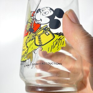 K&ouml;nnte beinhalten: Klares Glas mit einer Vintage-Mickey-Mouse-Angelszene. Mickey ist in einem roten Hemd und gelben Hosen dargestellt und h&auml;lt eine Angelrute. Das Glas hat einen gelb-gr&uuml;nen Hintergrund mit dem Text "WALT DISNEY PRODUCTIONS".