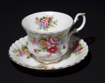 May include: A white porcelain teacup and saucer set featuring a scalloped edge and gold trim. The set is decorated with a colorful floral pattern of pink, red, yellow, and blue flowers with green leaves on the exterior and interior.