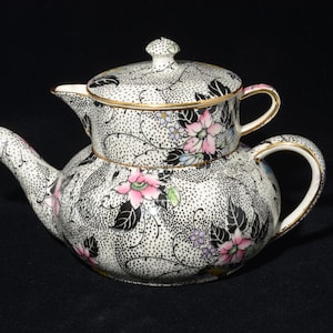 Peut inclure: Service à thé en céramique en deux parties avec un motif floral. L'ensemble présente un motif à pois noirs et blancs avec des accents floraux roses, noirs et verts. Une bordure dorée borde la théière et le couvercle.