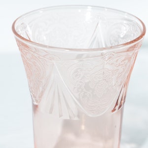 Pode incluir: Um copo de vidro transparente cor-de-rosa com um delicado padrão floral gravado no vidro.