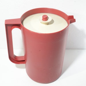 May include: A red plastic pitcher with a white lid and a red button on top. The pitcher has a handle and a spout.
