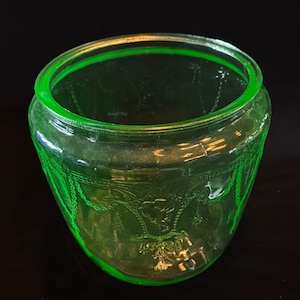 Könnte beinhalten: Eine grüne Glasdose mit einem dekorativen Design. Die Dose ist leer und hat eine abgerundete Form.