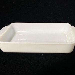 May include: A rectangular, white oven dish with rounded corners and two handles. The dish is made of a solid, opaque material. The design is simple and functional, suitable for baking. The dish is approximately 25 cm long.