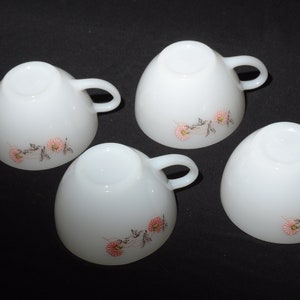 May include: Four white ceramic teacups with pink and black floral designs. The cups have a rounded shape and a handle on the side.