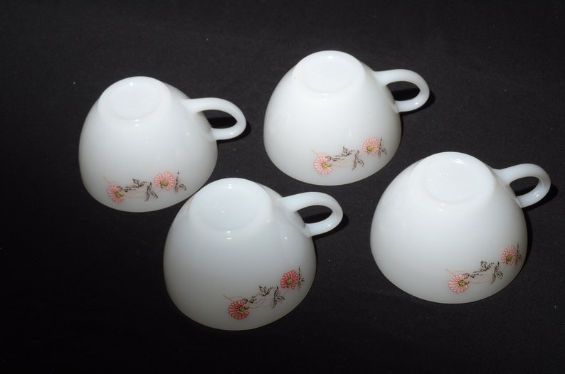 May include: Four white ceramic teacups with pink and black floral designs. The cups have a rounded shape and a handle on the side.