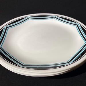 Puede incluir: Un juego de tres platos de cena de cerámica blanca con un diseño geométrico negro y turquesa alrededor del borde.
