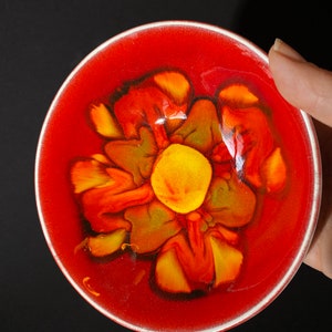 May include: A red ceramic bowl with a yellow, orange, and green flower design in the center.
