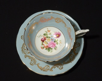 May include: A light blue teacup and saucer set with a floral design and gold trim. The cup and saucer have a scalloped edge.