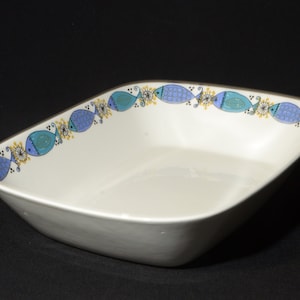 Può includere: Una pirofila in ceramica bianca con un motivo di pesci blu e gialli intorno al bordo.