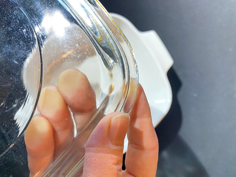K&ouml;nnte beinhalten: Nahaufnahme eines durchsichtigen Glasdeckels f&uuml;r eine Auflaufform. Der Deckel hat einen leicht abgerundeten Rand und wird von einer Hand gehalten.