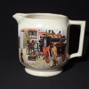 May include: A white ceramic pitcher with a handle, featuring a vintage illustration of a horse-drawn carriage with passengers and luggage. The scene is set in front of a building with a window.