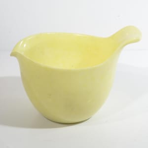 Könnte beinhalten: Eine hellgelbe Schüssel mit einem Ausgießer. Die Schüssel ist aus Glas und hat eine glatte, abgerundete Form.