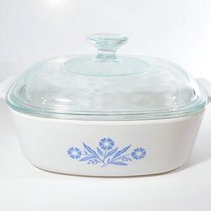 May include: White casserole dish with a clear glass lid and a blue floral design. The dish has a rounded shape with handles. The lid has a knob. A classic piece for baking and serving, perfect for the kitchen.