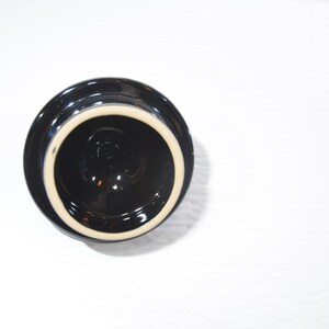 May include: Black ceramic lid with a white rim. The lid is round and has a smooth surface.