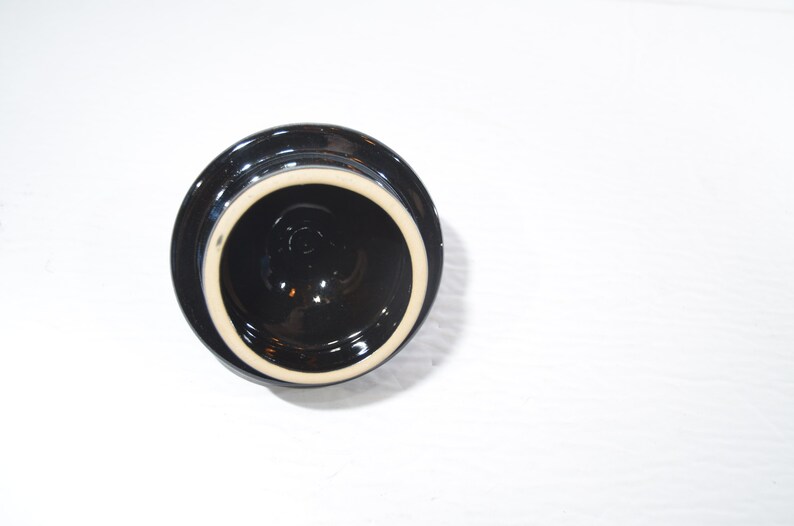 May include: Black ceramic lid with a white rim. The lid is round and has a smooth surface.