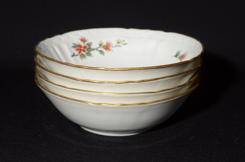 May include: Set of four white porcelain bowls with a floral design and gold trim. The bowls are stacked on top of each other.