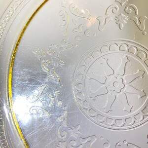 May include: A vintage glass plate with a yellow rim and a white floral design. The plate has a center design of a wheel with a flower in the middle.
