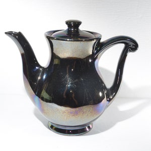 May include: A black iridescent ceramic teapot with a lid and a curved handle.